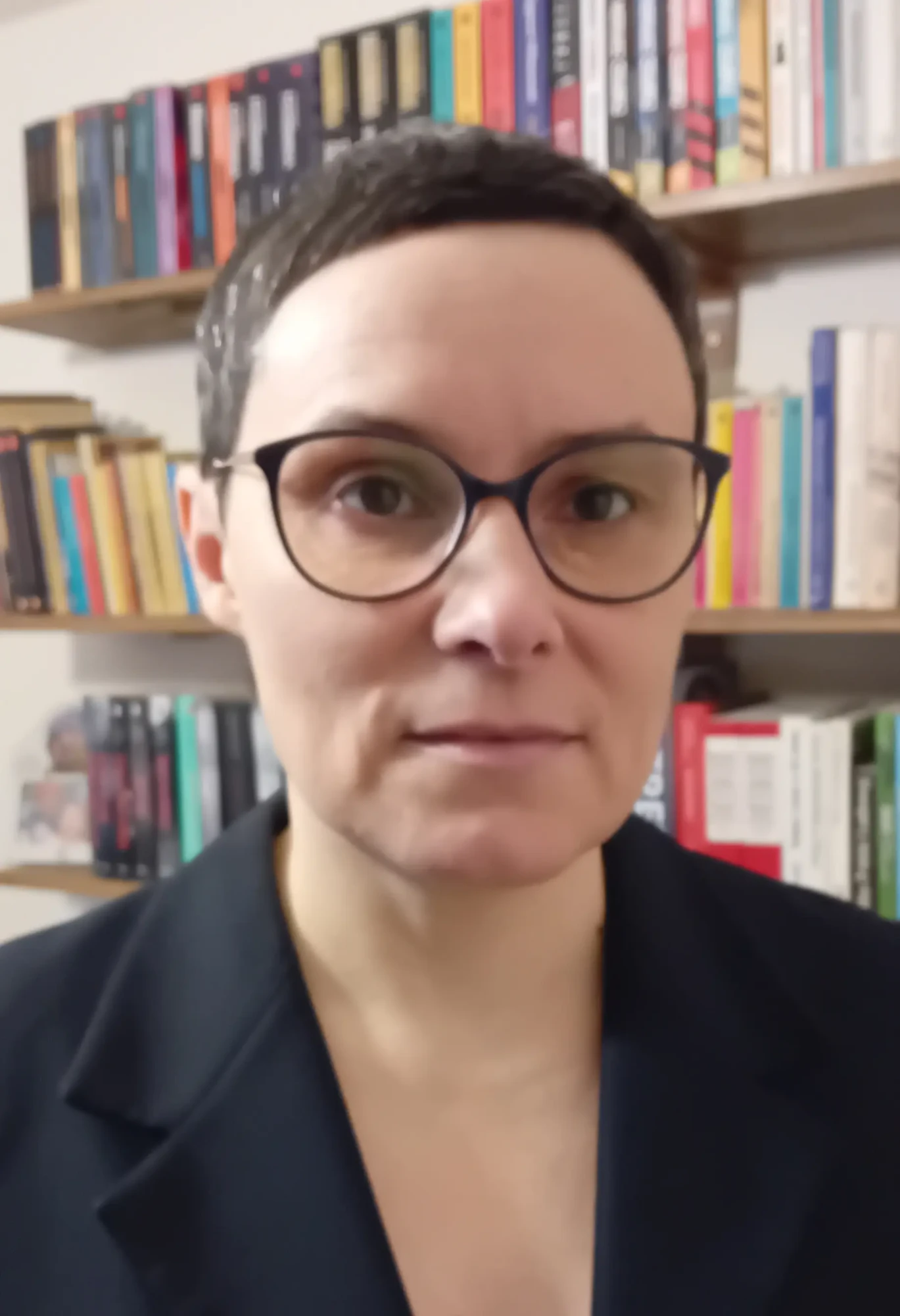 Zdjęcie portretowe kobiety z krótkimi włosami i okularami.