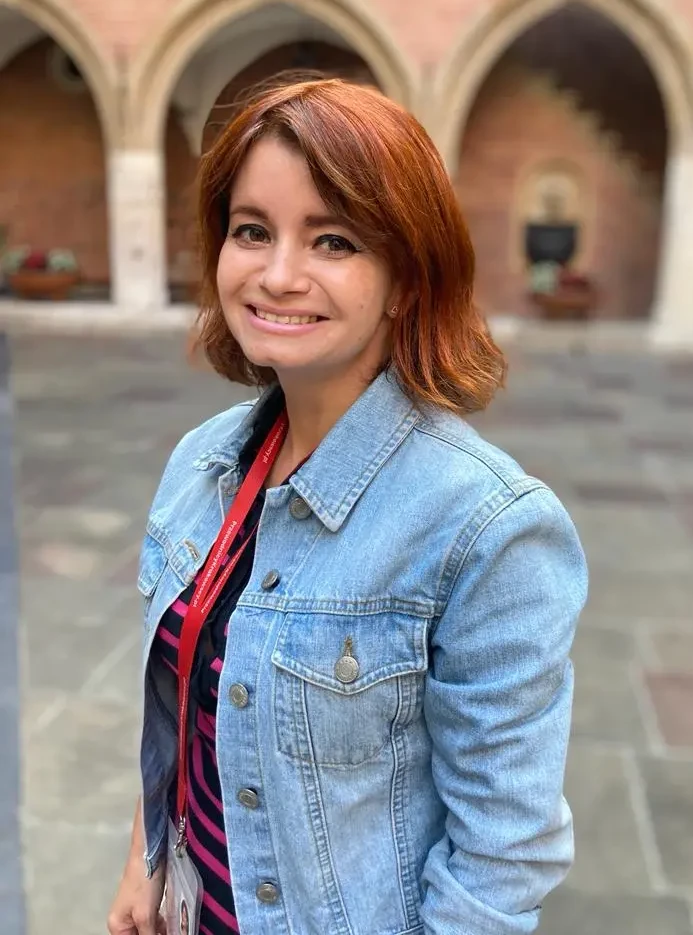 Zdjęcie potretowe kobiety, kobieta ma rude włosy, założoną bluzkę w paski i dżinsową kurtkę.