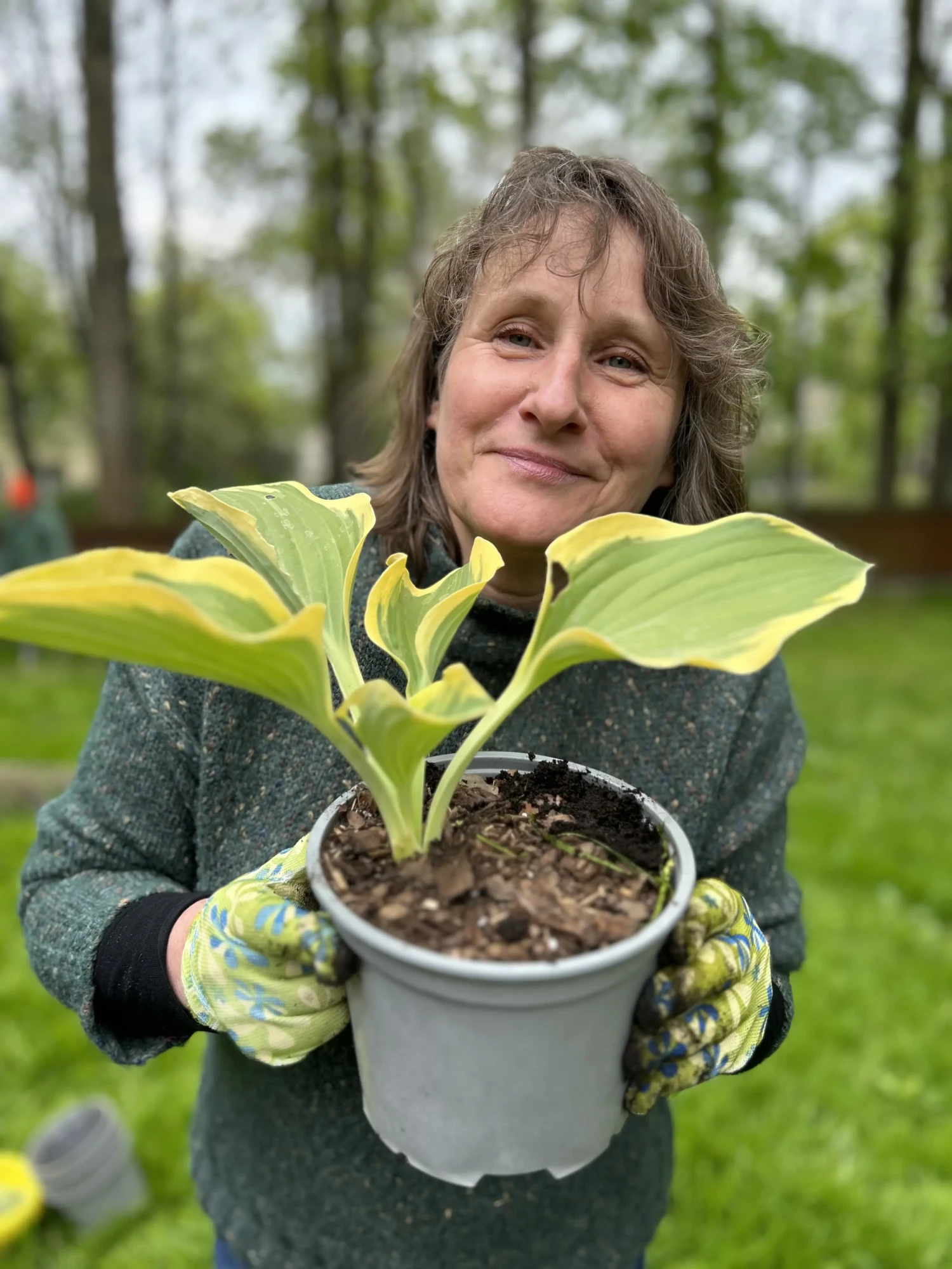Kobieta trzymająca w dłoniach doniczkę z kwiatem, uśmiechająca się do zdjęcia.