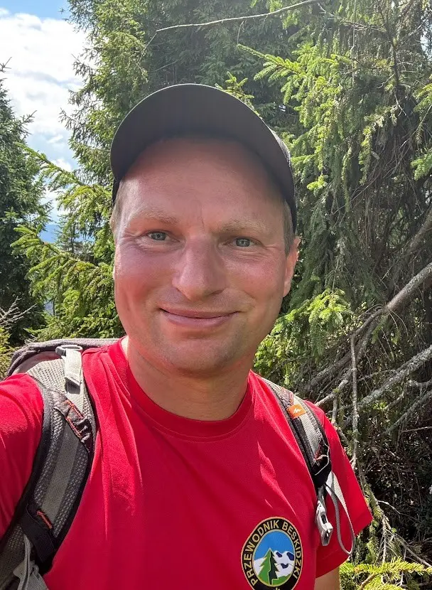 Mężczyzna w czerwonej koszulce z logo PTTK uśmiecha się do zdjęcia.