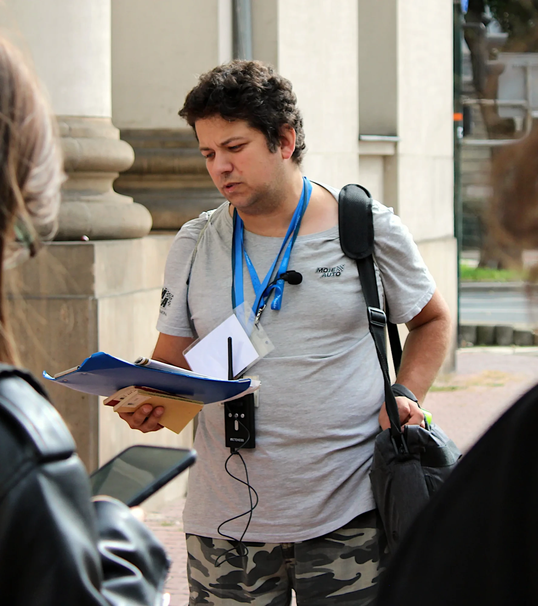 Przewodnik trzymający w ręce notatki, mówiący do ludzi.