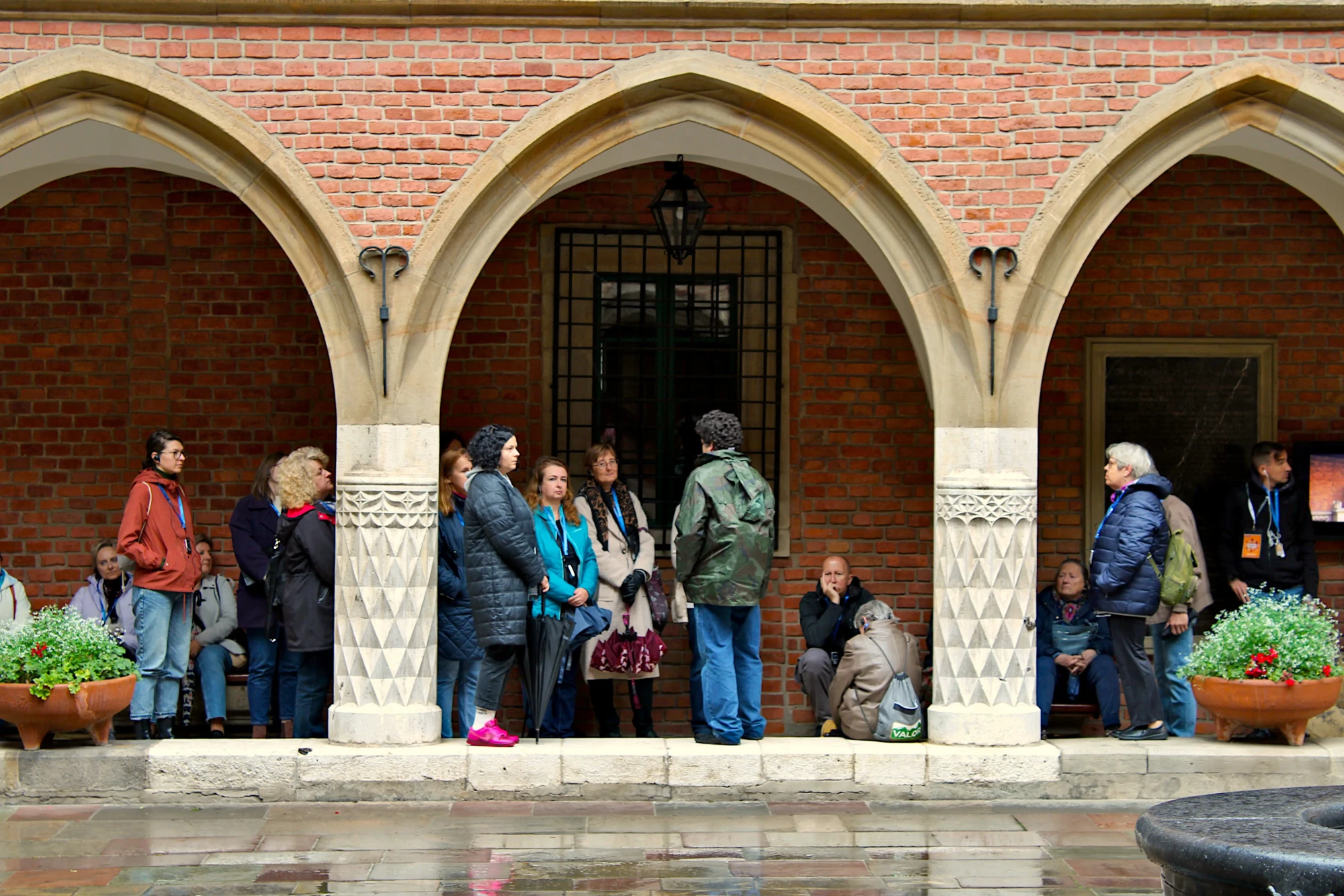 Grupa ludzi chowająca się przed deszczem w krużgankach Muzeum Uniwersytetu Jagiellońskiego Collegium Maius.