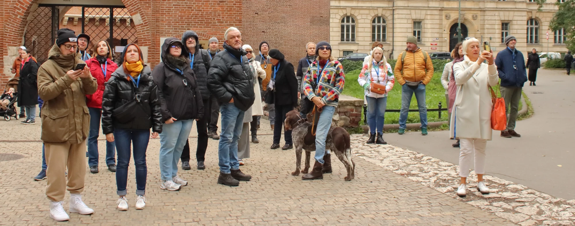Grupa ludzi przed Barbakanem patrzy w stronę Bramy Floriańskiej.