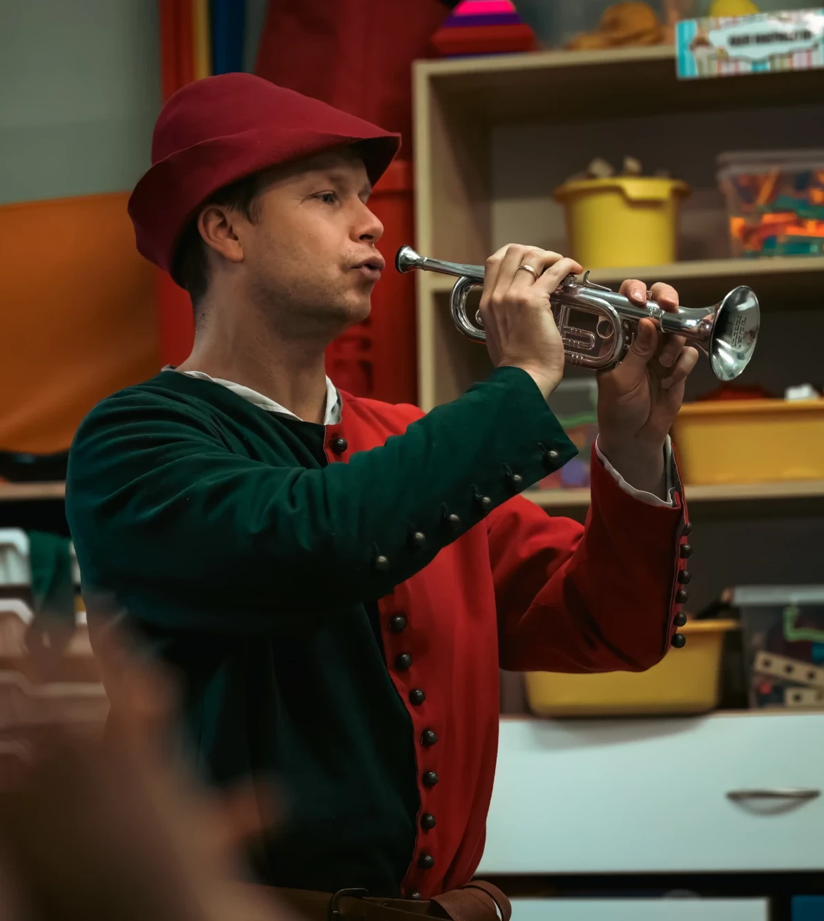 Mężczyzna w zielono-czerwonym stroju średniowiecznego grajka, udaje, że gra na trąbce.