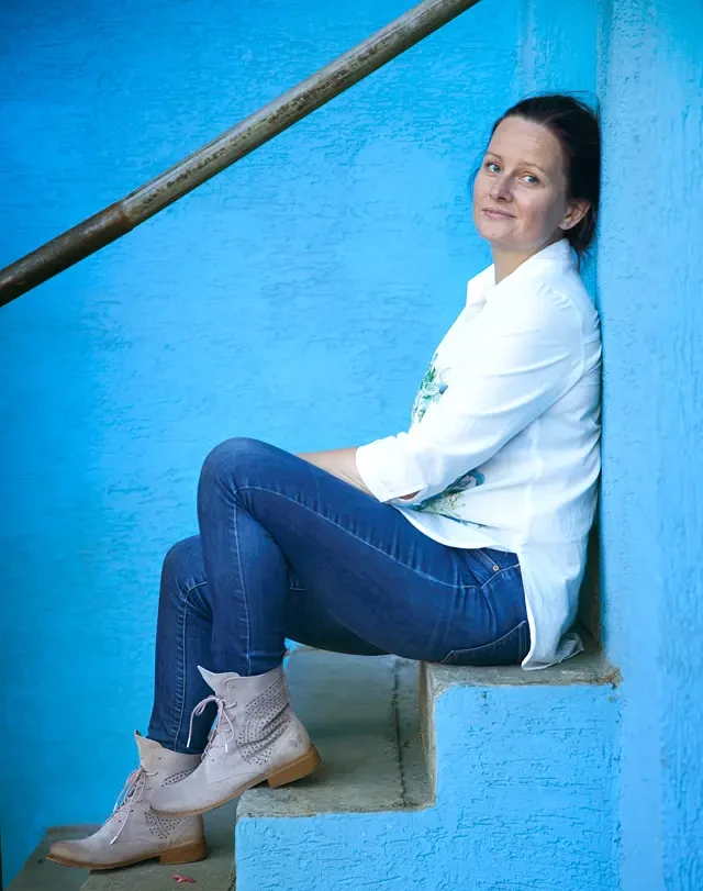 Kobieta siedząca na niebieskich schodach, uśmiechająca się w stronę obiektywu.