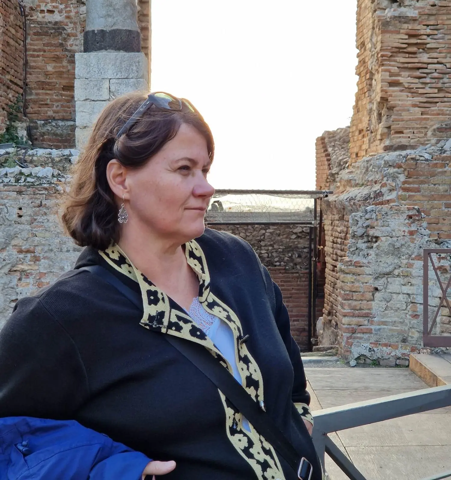 Zdjęcie kobiety z profilu, w tle ruiny.