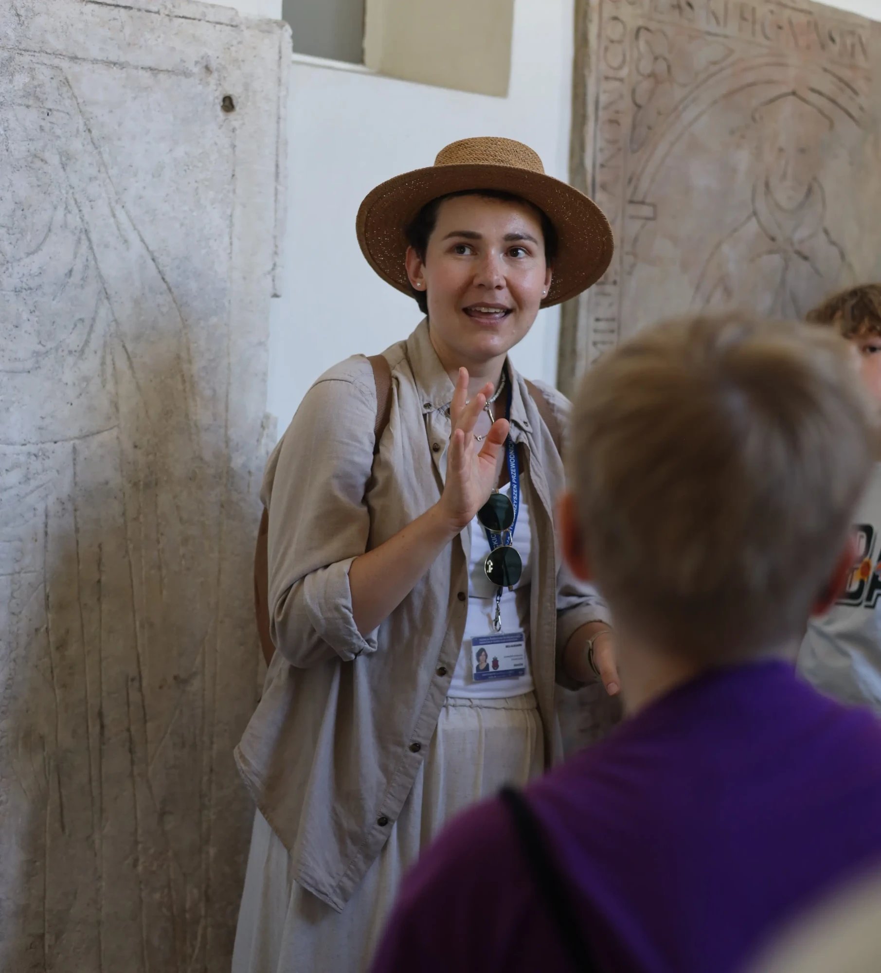 Przewodniczka w kapeluszu mówi do młodzieży.