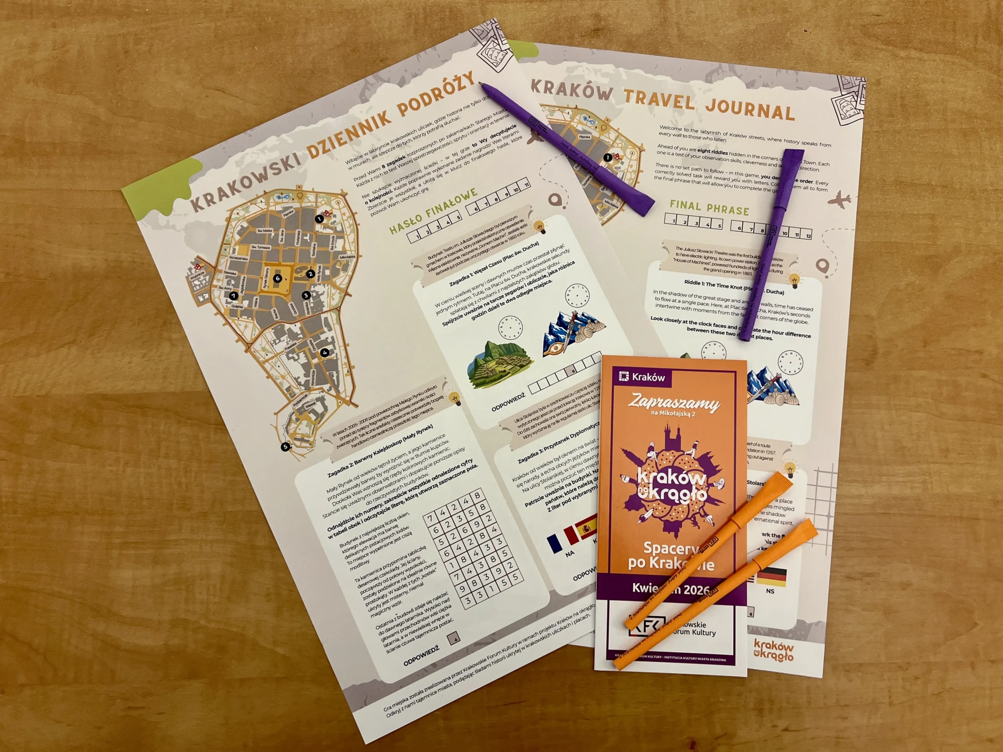 Quest w dwóch językach, ulotka z logo Kraków na okrągło i kolorowe długopisy na drewnianym blacie.